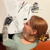 Lara Wilkin, Referentin des Weltkongresses, bringt ihre Erfahrungen aus der Armprothetik in Forschung und Praxis ein. Zur Eröffnung zeigt sie eine mit ihrer Prothesenhand im Februar 2026 erstellte Zeichnung, die ihre Perspektive auf 50 Jahre OTWorld sichtbar macht. 