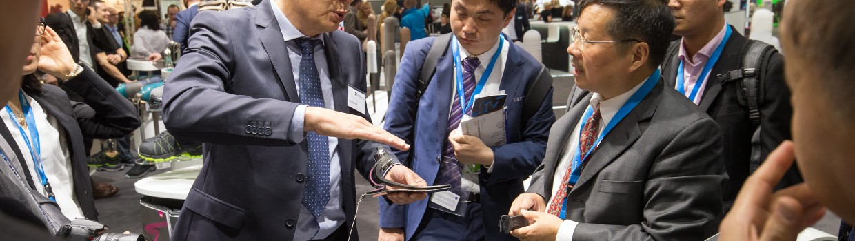 Ein Mann im Anzug erklärt einer Gruppe von Messebesuchern ein technisches Produkt an einem Ausstellungsstand. Ein Mann im Anzug erklärt einer Gruppe von Messebesuchern ein technisches Produkt an einem Ausstellungsstand.