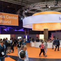 Besucherinnen und Besucher bewegen sich durch das Congress Center der OTWorld mit orangem Boden und einem großen runden Informationsstand, darüber ein Schild mit Hinweisen auf Kongresstaschen und Tickets; links hängt ein großes Banner mit der Aufschrift „Congress Center OTWorld“.