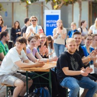 Viele junge Menschen sitzen an einem Tisch applaudierend und lachend.  Viele junge Menschen sitzen an einem Tisch applaudierend und lachend.
