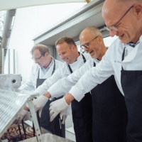 Vier Männer stehen an einem Grill.  Vier Männer stehen an einem Grill.