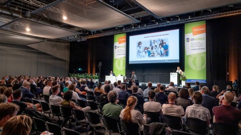 Kongresssituation: Auf der Bühne im Kongresssaal läuft ein Vortrag, davor sitzen zahlreiche Zuhörer.