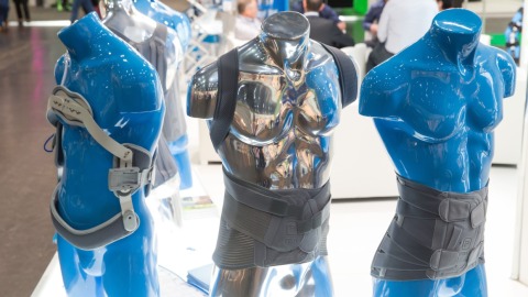 Three blue torso mannequins wearing orthopedic back and torso braces at a trade fair booth.