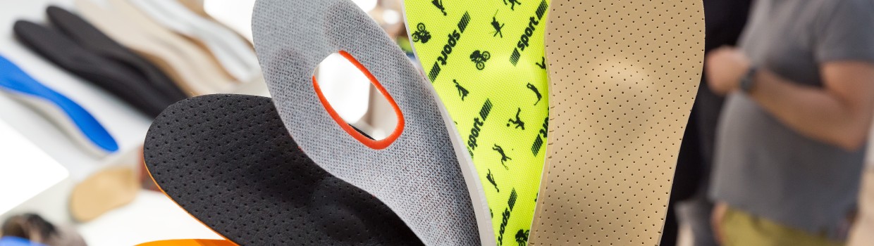 A hand holds five differently designed insoles fanned out at OTWorld; in the background, more insoles are laid out on tables and people are seen in conversation. A hand holds five differently designed insoles fanned out at OTWorld; in the background, more insoles are laid out on tables and people are seen in conversation.