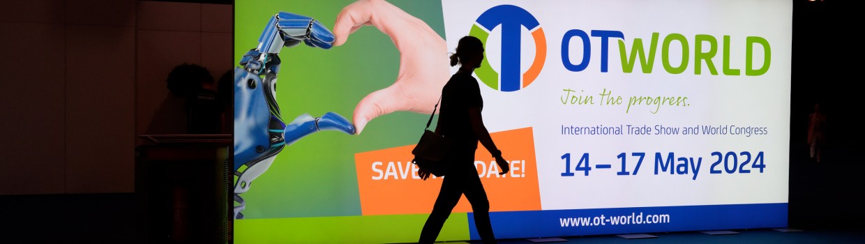 A person walks past an illuminated OTWorld promotional sign displaying the date and slogan.