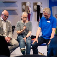 A woman with a microphone sits between two men and talks about compression stockings. A woman with a microphone sits between two men and talks about compression stockings.