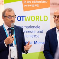 Two men stand in front of a roll-up display showing the OTWorld logo. Two men stand in front of a roll-up display showing the OTWorld logo.