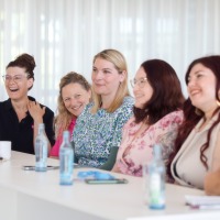 Group of six participants sitting smiling at a conference table, with water bottles and notes in front of them. Group of six participants sitting smiling at a conference table, with water bottles and notes in front of them.