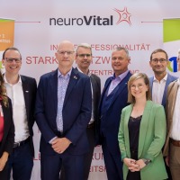 Group photo of nine professionals in front of the OTWorld and neuroVital banners, smiling and in business attire. Group photo of nine professionals in front of the OTWorld and neuroVital banners, smiling and in business attire.