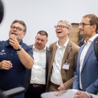 Group of professionals at OTWorld enthusiastically watching a product demonstration, several people smiling and engaged in conversation. Group of professionals at OTWorld enthusiastically watching a product demonstration, several people smiling and engaged in conversation.
