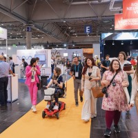Group of visitors moving between exhibitor stands, including one person on an e-scooter Group of visitors moving between exhibitor stands, including one person on an e-scooter