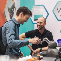 A trade fair visitor tests a technical assistance system at the exhibition stand while an exhibitor watches with a smile. A trade fair visitor tests a technical assistance system at the exhibition stand while an exhibitor watches with a smile.