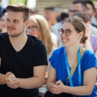 Young man and young woman standing in the audience smiling and applauding at an event. Young man and young woman standing in the audience smiling and applauding at an event.