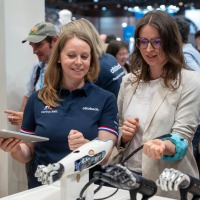 Two women look at a prosthetic arm. Two women look at a prosthetic arm.