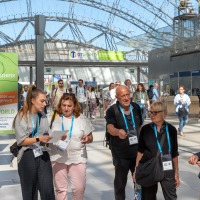 Group of visitors with lanyards walk through the glass hall of the Leipzig Trade Fair, next to a sign with the motto 'You make the difference! Group of visitors with lanyards walk through the glass hall of the Leipzig Trade Fair, next to a sign with the motto 'You make the difference!