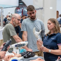 Exhibitor demonstrates a modern hand prosthesis at OTWorld while several visitors listen attentively and examine other prosthetic models. Exhibitor demonstrates a modern hand prosthesis at OTWorld while several visitors listen attentively and examine other prosthetic models.