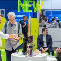 Two men examining new prosthetic components at a display table at OTWorld, with a glowing ‘NEW’ sign above. Two men examining new prosthetic components at a display table at OTWorld, with a glowing ‘NEW’ sign above.