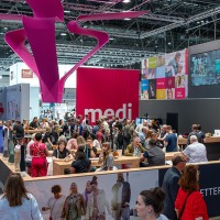 Numerous trade fair visitors gather at the colorful medi booth at OTWorld, with a large pink sculpture suspended above Numerous trade fair visitors gather at the colorful medi booth at OTWorld, with a large pink sculpture suspended above