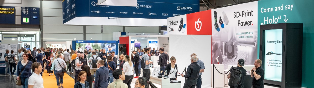 Full exhibition hall at OTWorld with visitors walking along an orange carpet path past exhibition stands