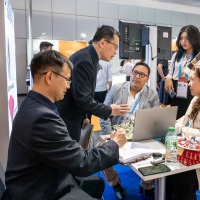 Business meeting at an OTWorld trade fair booth, with five people intently discussing documents and color samples around a small table Business meeting at an OTWorld trade fair booth, with five people intently discussing documents and color samples around a small table