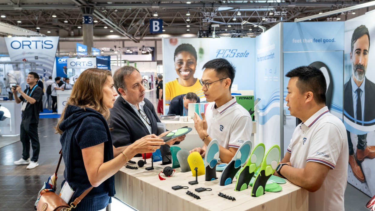 Two visitors discussing colorful orthopedic insoles with exhibitors at a trade fair booth at OTWorld Two visitors discussing colorful orthopedic insoles with exhibitors at a trade fair booth at OTWorld