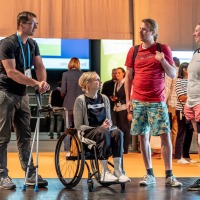 Four visitors with mobility aids and prostheses engage in conversation in a relaxed atmosphere at OTWorld. Four visitors with mobility aids and prostheses engage in conversation in a relaxed atmosphere at OTWorld.