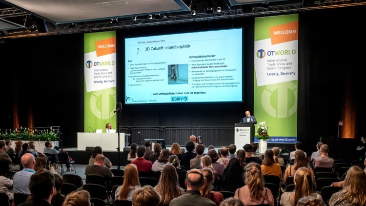A lecture event at OTWorld in Leipzig. Numerous attendees are seated in the audience, watching a speaker present on stage. A large screen displays a slide with information, flanked by two OTWorld banners.